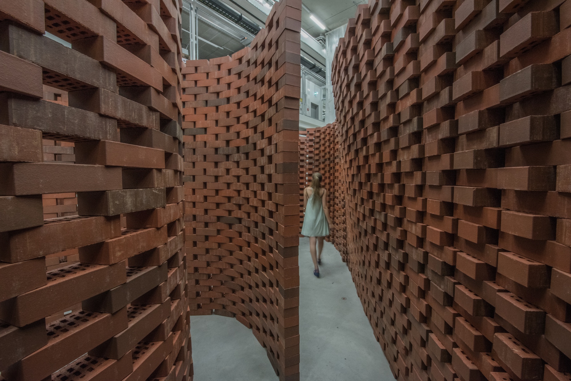 inside the Brick Labyrinth installations, with one brick wall on each side, option to turn to left or go on by the right as a person walks through 